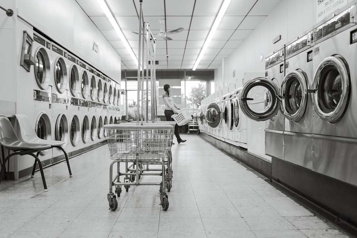 Salle de blanchisserie avec machines à laver, chariot et personne Salle de blanchisserie avec machines à laver, chariot et personne