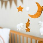 Berceau avec mobiles en bois et moutons en peluche, coussins blancs sur un mur gris