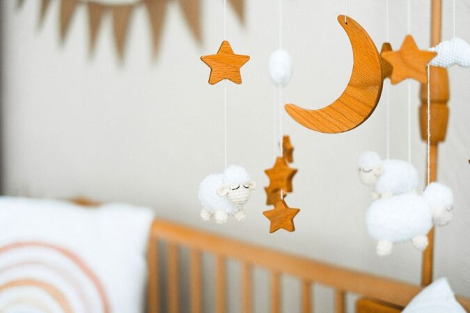 Berceau avec mobiles en bois et moutons en peluche, coussins blancs sur un mur gris