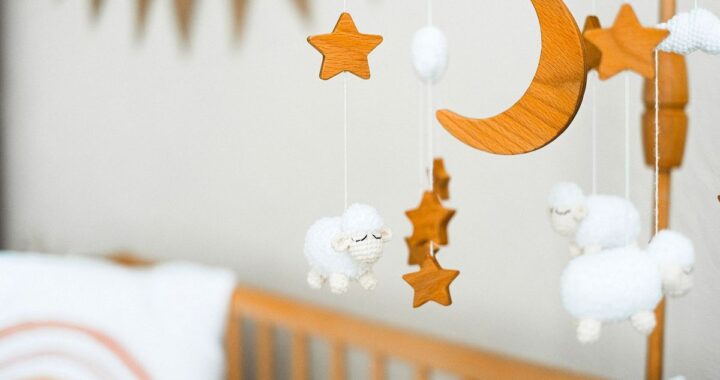 Berceau avec mobiles en bois et moutons en peluche, coussins blancs sur un mur gris