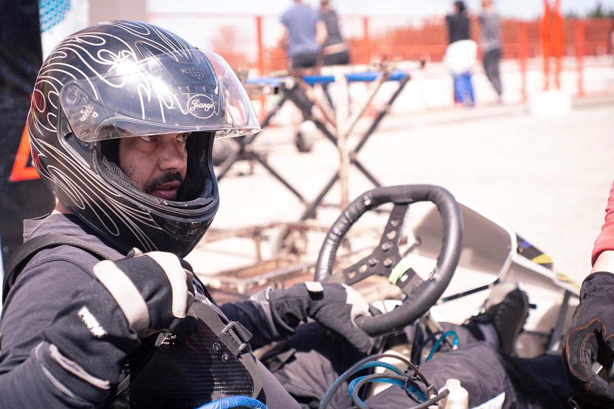 Un coureur en casque noir tient le volant d'un kart sur piste