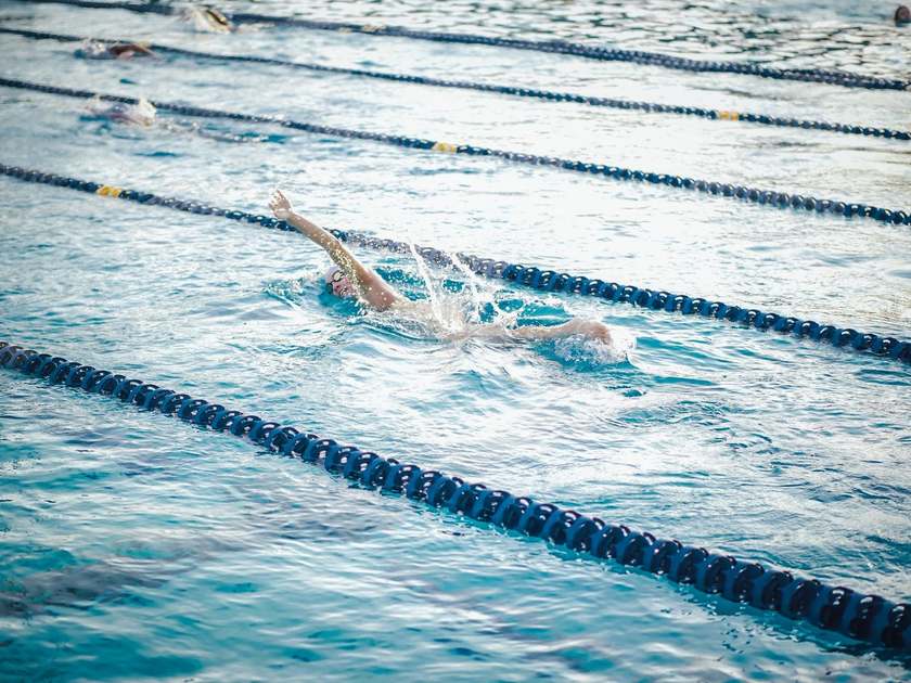 Nageur en pleine course dans une piscine, bras levé, eau en mouvement Nageur en pleine course dans une piscine, bras levé, eau en mouvement