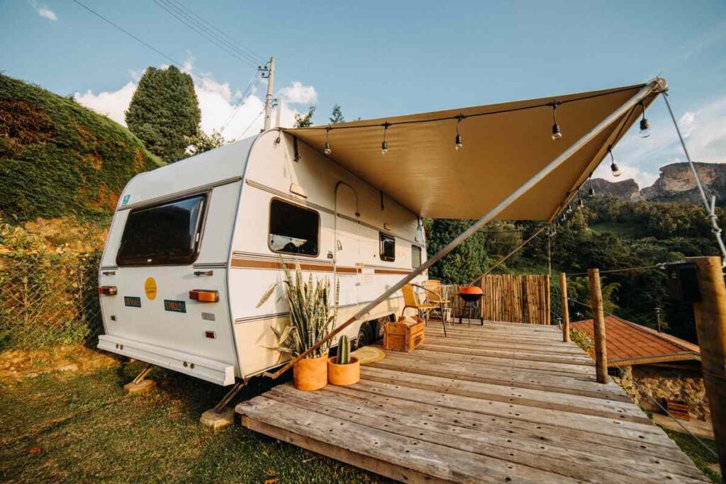 Caravelle blanche avec auvent sur terrasse en bois, jardin et montagnes sous ciel clair