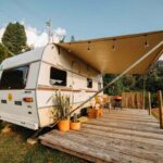 Caravelle blanche avec auvent sur terrasse en bois, jardin et montagnes sous ciel clair