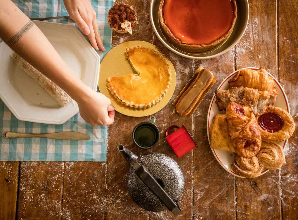 Main plaçant un plat sur une table en bois avec desserts et ustensiles Main plaçant un plat sur une table en bois avec desserts et ustensiles