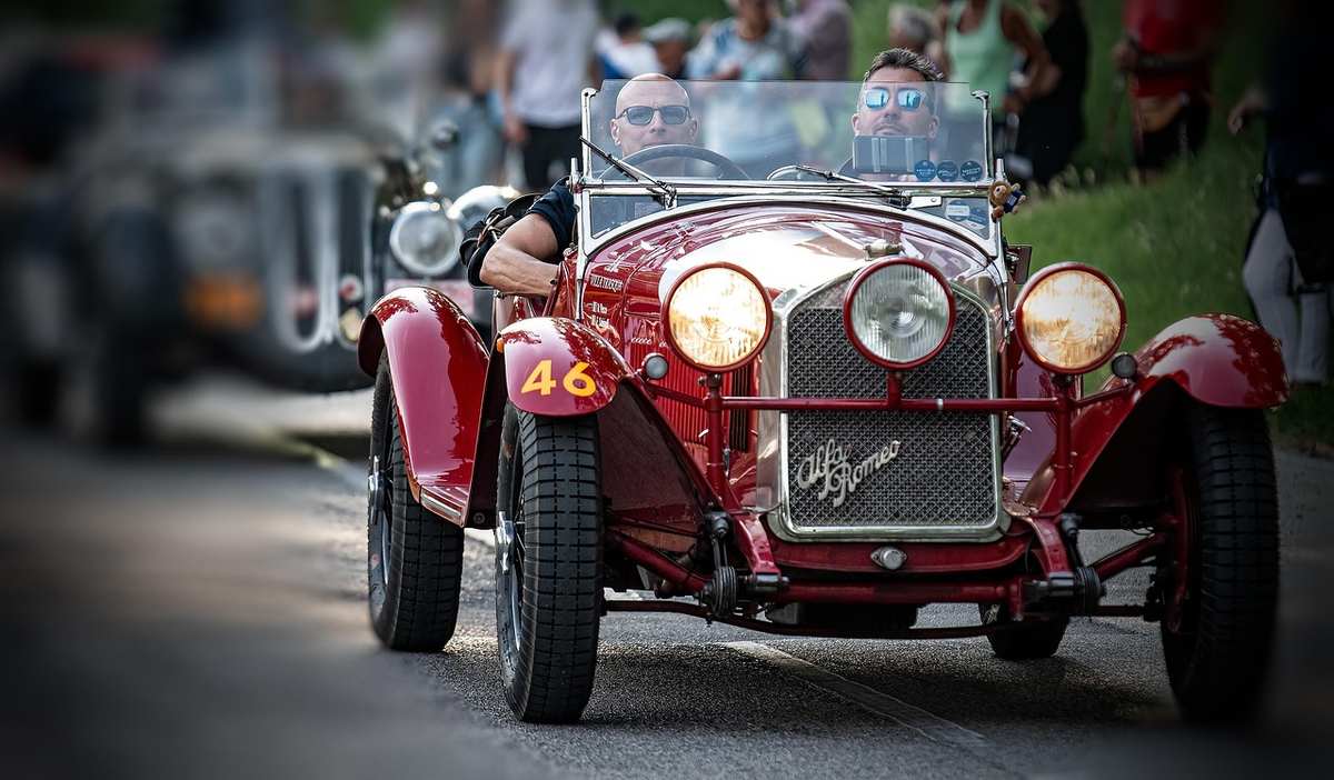 Une voiture rouge vintage conduit sur une route avec des spectateurs Une voiture rouge vintage conduit sur une route avec des spectateurs