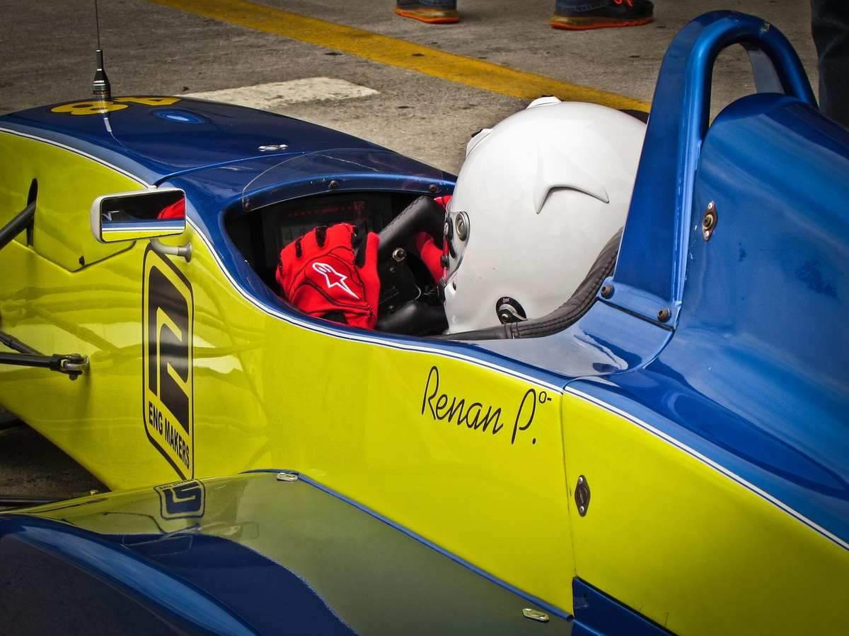 Pilote assis dans une voiture de course jaune et bleue, casque blanc