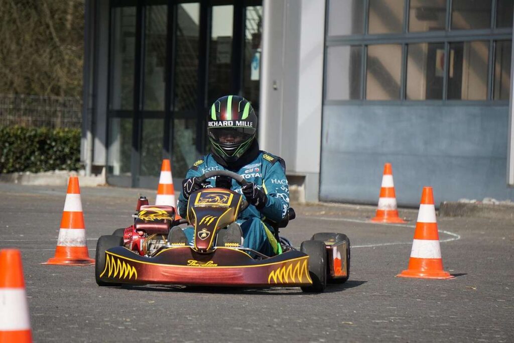 Un pilote en karting avec casque conduit un kart rouge entre cônes orange