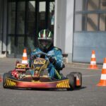 Un pilote en karting avec casque conduit un kart rouge entre cônes orange