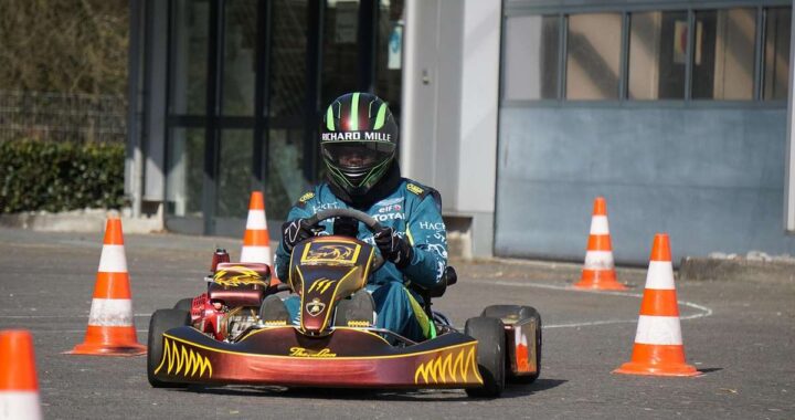 Un pilote en karting avec casque conduit un kart rouge entre cônes orange